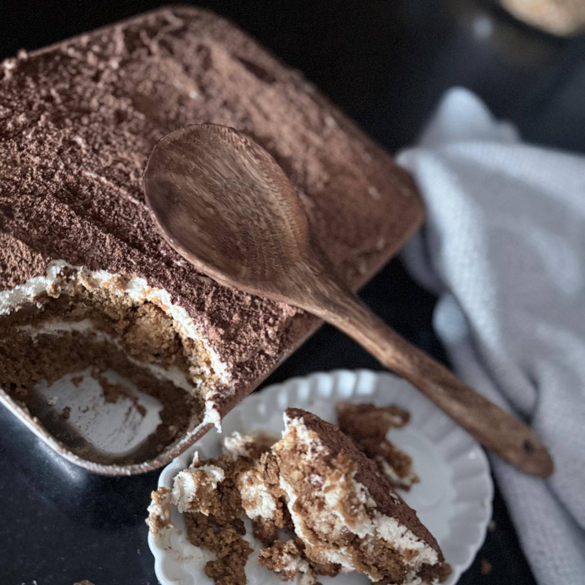 Tiramisu dessert with a wooden spoon on a dark surface
